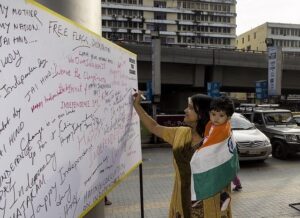 Indian woman writing a patriotic message on Republic Day wall while holding a child wrapped in the Indian national flag